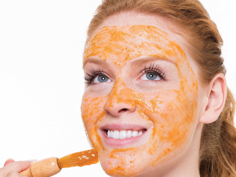 Fille avec un pinceau met un masque de carottes sur son visage
