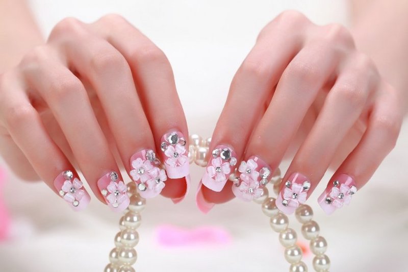 Jasny różowy manicure z akrylowymi kwiatami i kryształkami.
