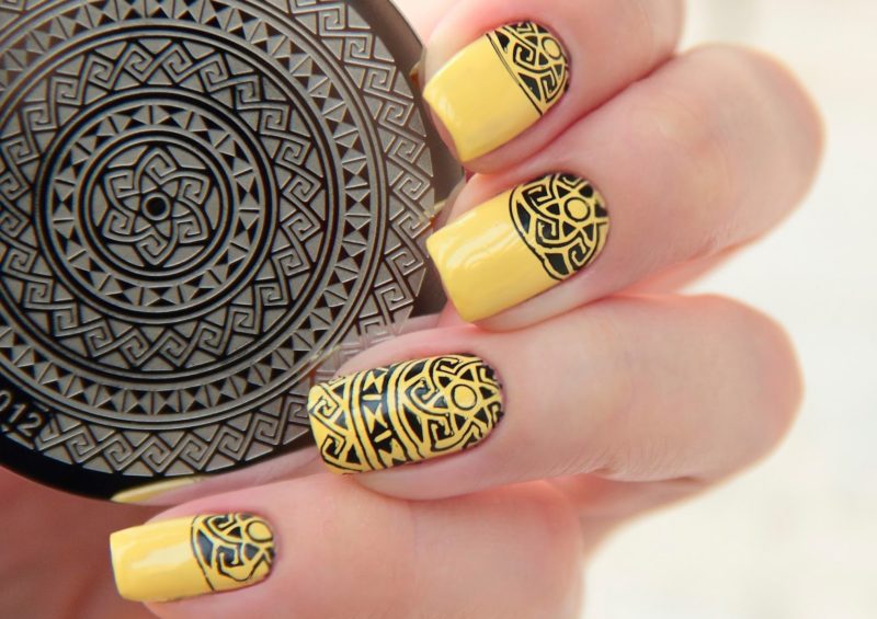 Gele manicure met zwart etnisch zegelpatroon.