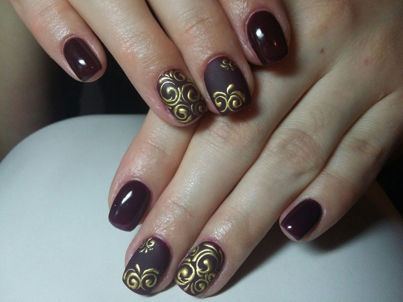 Burgundiczny manicure ze złotymi monogramami.