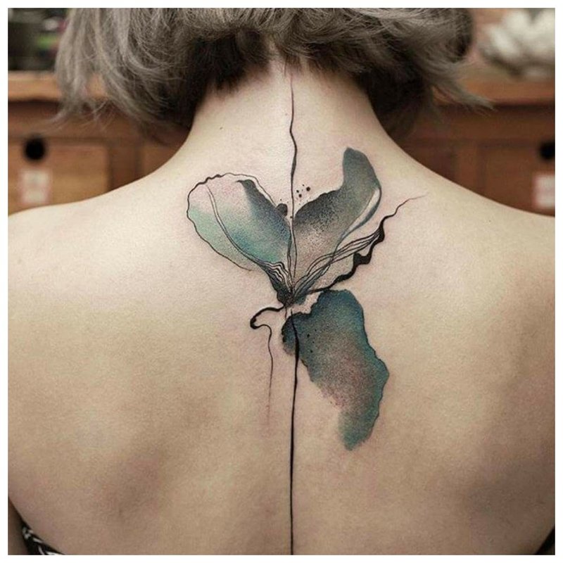 Aquarel tattoo in de vorm van een bloem tussen de schouderbladen